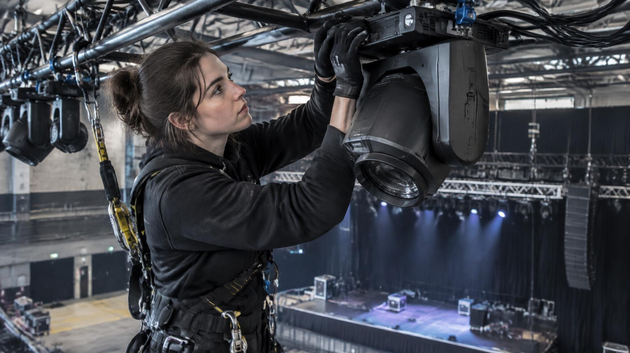 Lighting technician adjusting a stage lighting fixture on a rig